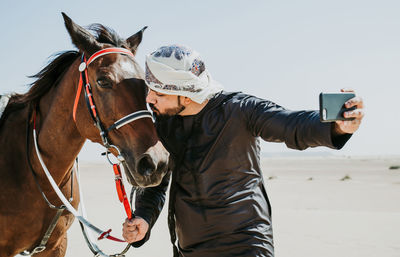 Man kissing horse while taking selfie with smart phone