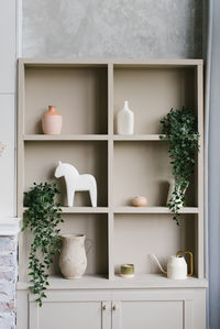 Open cabinet with shelves decorated with vases and indoor plants in scandinavian style