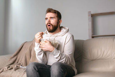 Man looking away while sitting on sofa at home