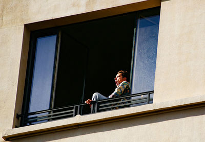 Low angle portrait of woman standing by window against building
