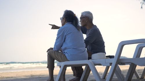 Happy asian family, senior couple sitting on chairs with backs on beach travel vacation