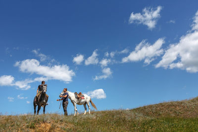 Woman riding horse with friend on field against sky