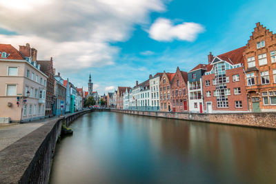 Canal amidst buildings in city against blue sky