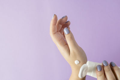 Cropped hand of woman holding moisturizer against purple background