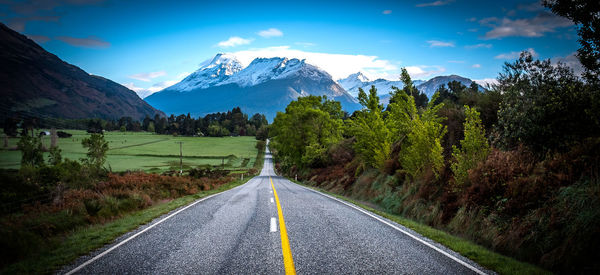 Empty road by field leading towards mountain