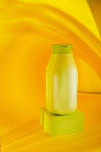 Close-up of yellow bottle on table against wall