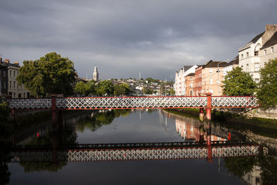 Bridge over river by buildings in city against sky