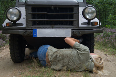 Rear view of woman repairing vehicle on dirt road