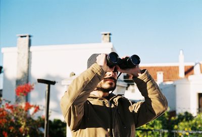 Man using binoculars while standing against building