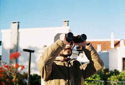 Man using binoculars while standing against building