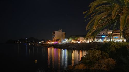 Illuminated buildings by sea against sky at night