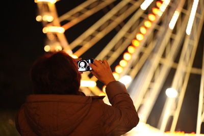 Close-up of woman photographing illuminated ferris wheel using smart phone at night