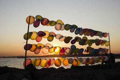 Multi colored balloons on rocks against sea during sunset