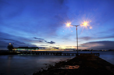 Illuminated street light on pier over sea against sky at dusk