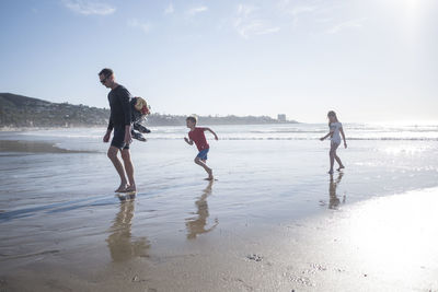 Full length of father with children enjoying vacation at beach on sunny day