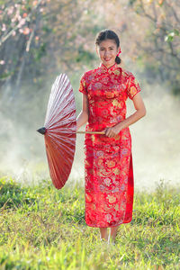 Portrait of woman with red umbrella standing on field