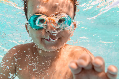 Underwater view of positive boy in goggles swimming in clean water in pool while having fun at weekend in summer