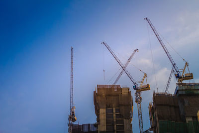 Low angle view of cranes at construction site against sky