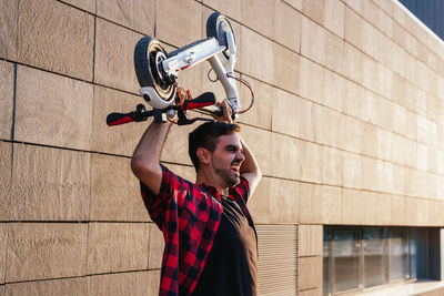 Young man with bicycle standing against wall