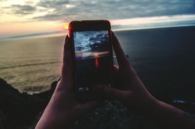 Cropped hands of woman photographing sea against sky