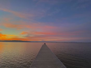 Scenic view of couple on pier on lake against sky during sunset