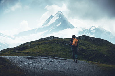 Rear view of man standing on snowcapped mountain against sky