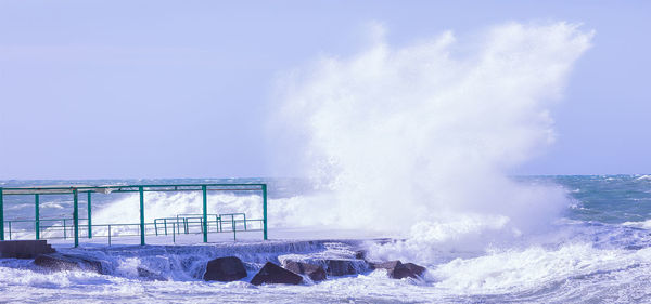 Waves breaking against sea against clear sky