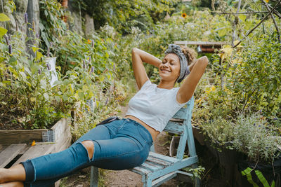 Smiling female farmer with hands behind head resting in urban garden