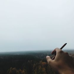 Close-up of person holding cigarette against sky