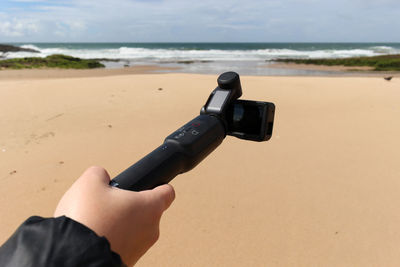 Cropped image of hand holding digital video camera at beach