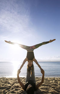 Determined multi-ethnic couple doing yoga on shore against sky