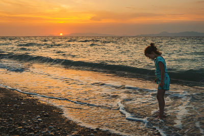 Woman standing on beach against sky during sunset