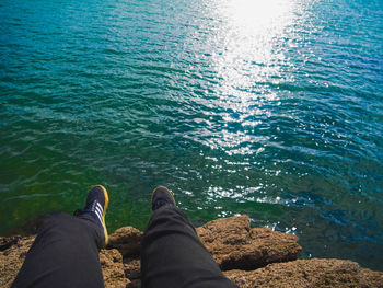 Low section of man relaxing on rock by sea