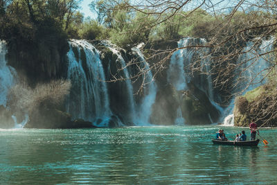 People rowing boat on river against trees