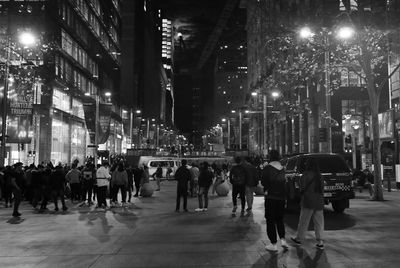 People walking on illuminated street amidst buildings in city at night