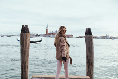 Smiling young woman standing on pier over canal in city