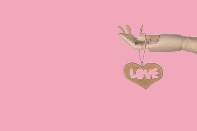 Close-up of hand holding heart shape against pink background