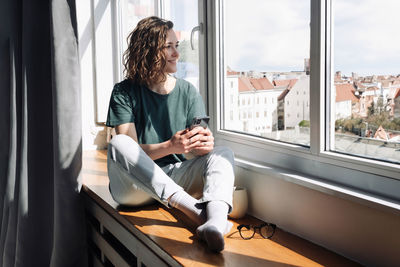 Digital detox. serene young woman embracing relaxation at home, gazing out of window, disconnecting