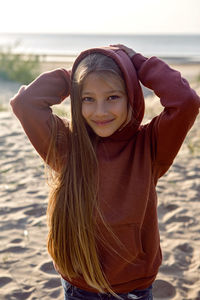 Portrait of a girl with long hair standing on a sandy beach in a hoodie and hood