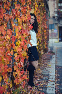 Portrait of young woman standing amidst creeper plants during autumn