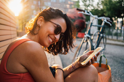 Close-up of smiling woman using mobile phone while sitting outdoors