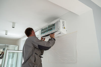 Male worker installing air conditioner in apartment during summer season.