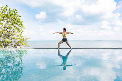 Woman exercising against sea at infinity pool