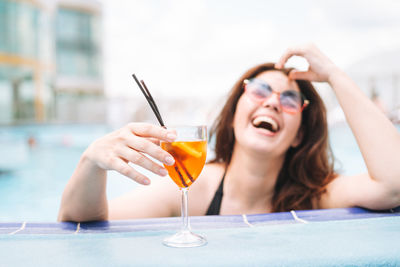 Stylish young woman plus size body positive in sunglasses enjoying life with cocktail in pool