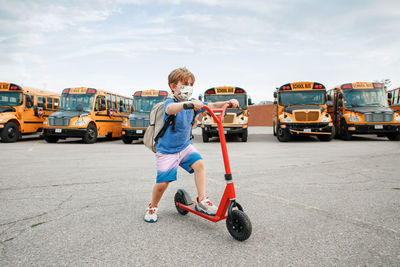 Boy in face protective mask riding scooter on school yard. education and back to school 