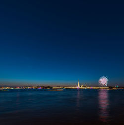 Illuminated city by sea against clear blue sky at night