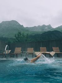 Shirtless man swimming in pool against mountains