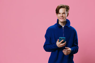 Portrait of young woman standing against pink background