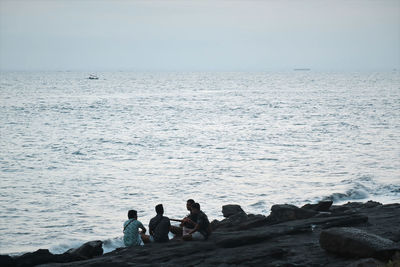 People on rocks by sea against sky