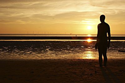 Silhouette man standing at beach against sky during sunset